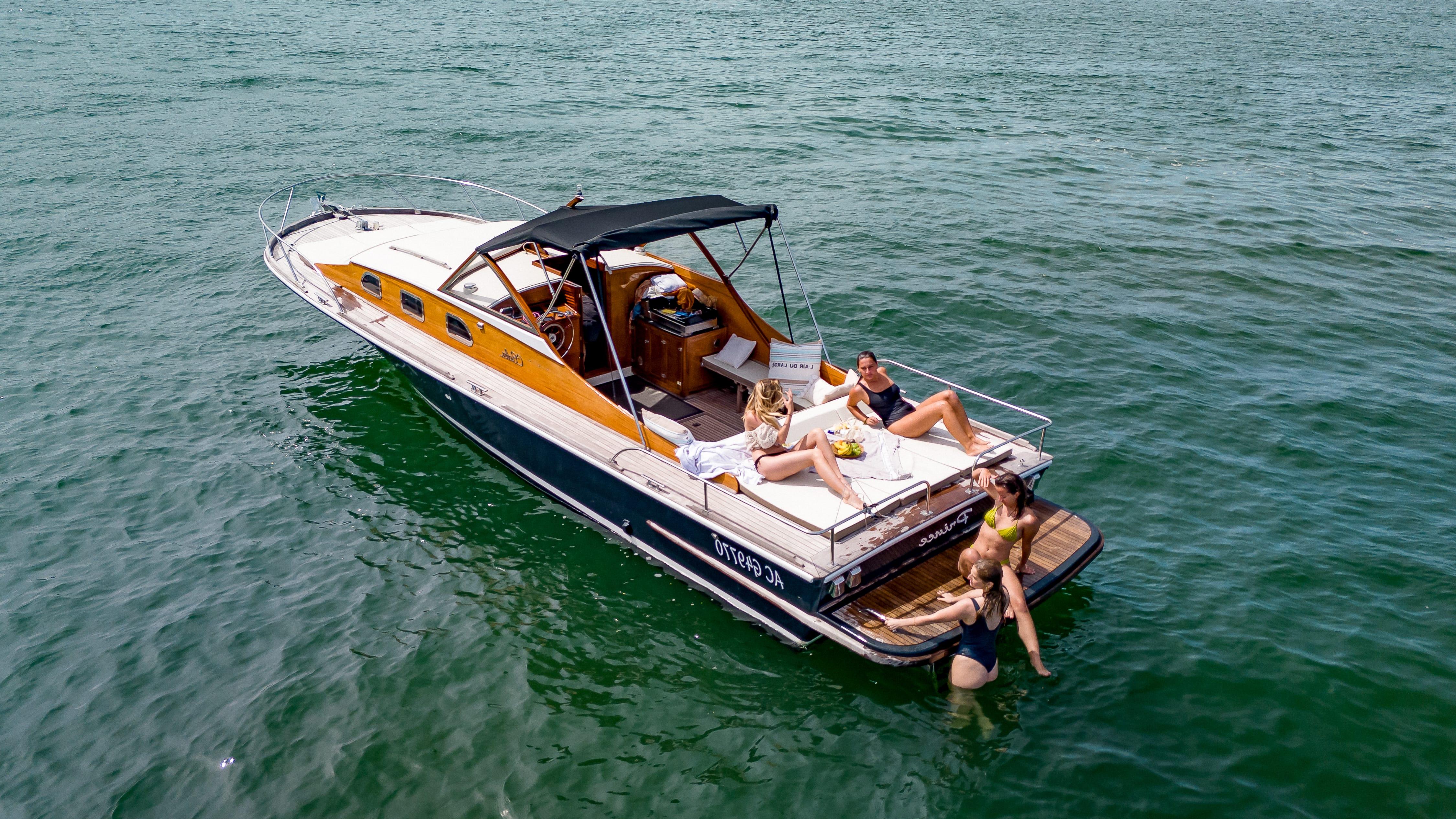 Raba boat with yellow hull and teak deck, holidaymakers relaxing on board and a person swimming in the calm waters of the Arcachon Basin.