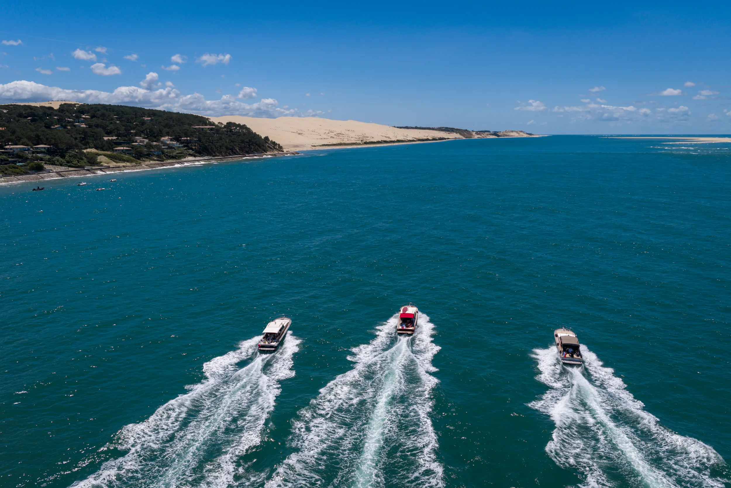 Trois pinasses naviguant de front vers la Dune du Pilat, vues du ciel.
